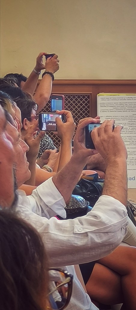 Persone in una sala che usano telefoni per fotografare durante un evento.