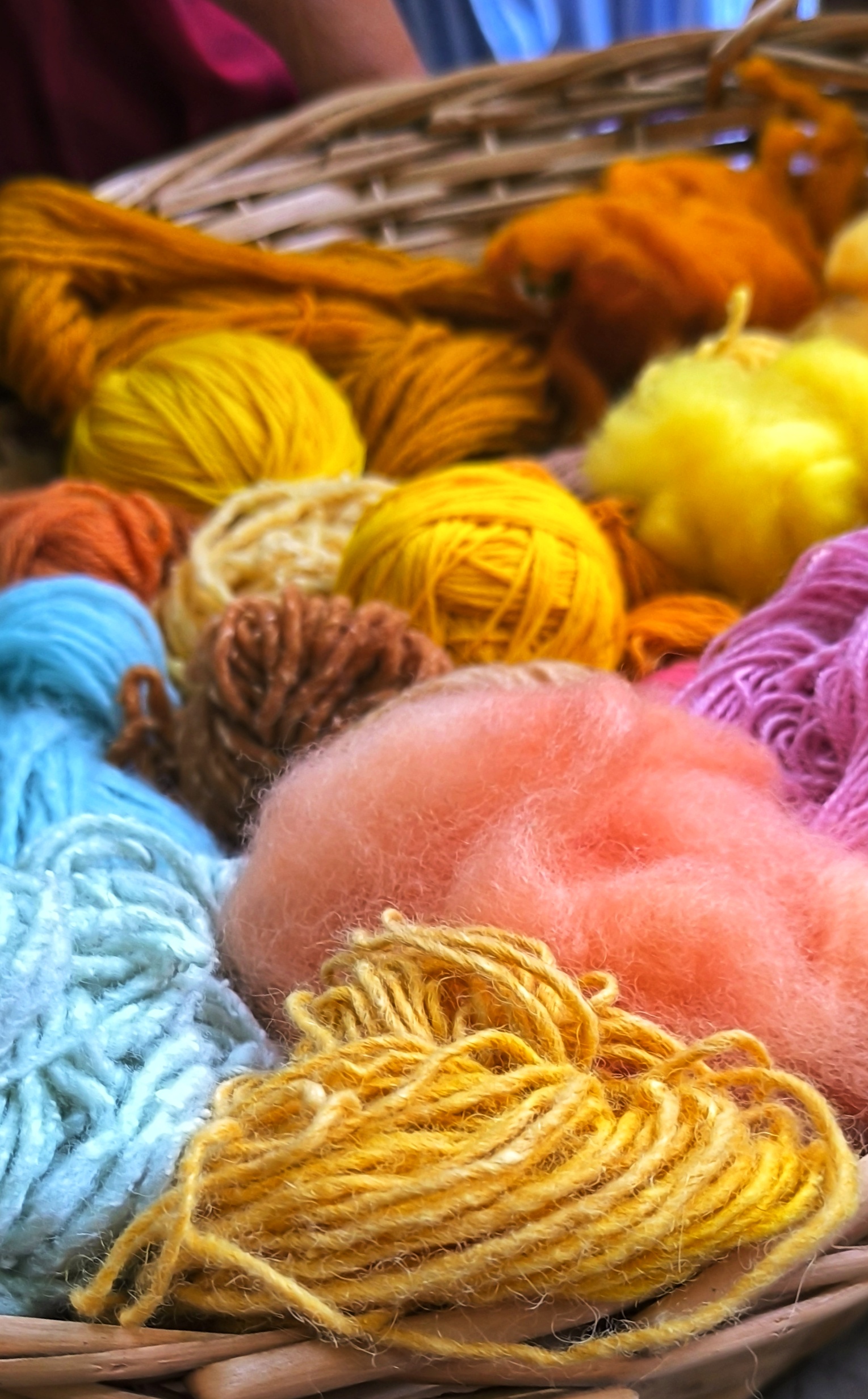 Un cesto pieno di gomitoli di filato colorato, tra cui giallo, arancione, blu e rosa.