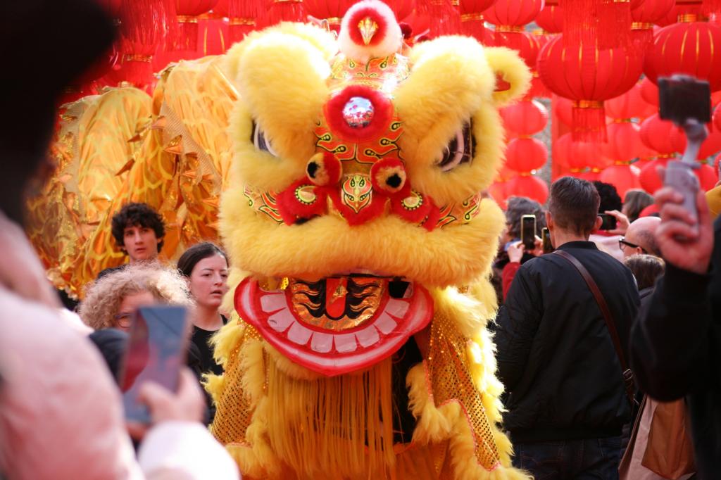 Un gruppo di persone osserva una danza del drago cinese durante una celebrazione, con lanterne rosse sullo sfondo.